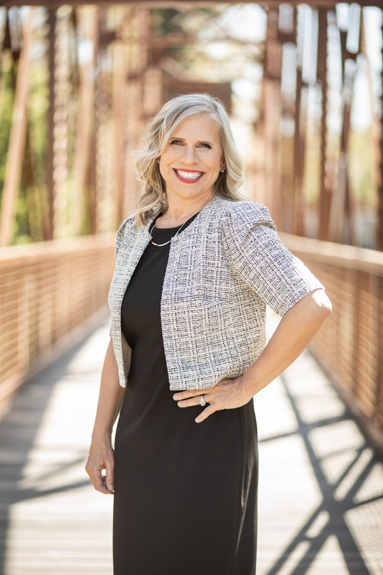 Melissa A. Washington standing on a wooden footbridge in a black dress and textured jacket